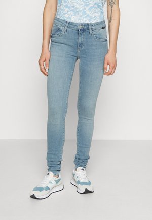Jeans ajustados de color azul con un lavado medio, diseño de cinco bolsillos, que presentan un ligero desgastado. Combinados con unas zapatillas de deporte azul claro y una blusa con estampado.