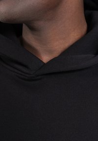 Schwarzer Hoodie mit entspannter Halslinie, geripptem Muster und sichtbaren Nähten entlang der Kanten, der Komfort und lässigen Stil betont.