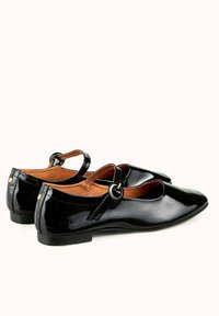 Ballerines en cuir verni noir avec un bout rond, une bride de cheville dotée d'une boucle circulaire et une semelle intérieure en cuir tan. Design à talon plat.