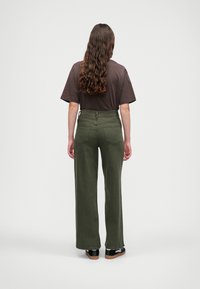 Olivově zelené široké kalhoty s kapsami na zadní straně, kombinované s hnědým tričkem s krátkým rukávem. Texturovaná tkanina, casual design.