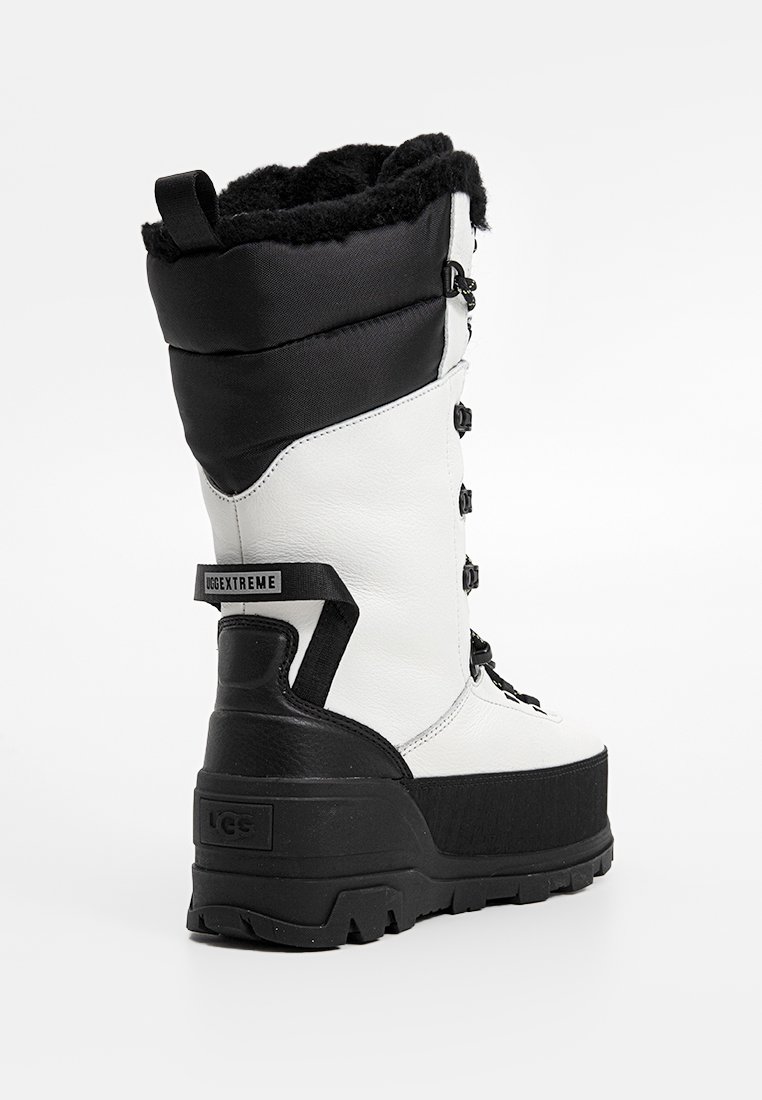 Weiße und schwarze hochhackige Schneestiefel mit einer strukturierten Oberfläche, Kunstfellkragen und einer robusten Gummisohle mit Fersenverstärkung.