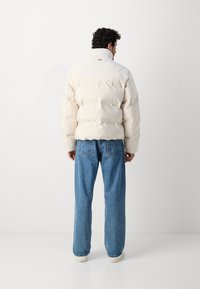 Pūkinis džemperis off-white spalvos, su aukštu apykakle, siuvinėta tekstūra ir laisvu kirpimu, derinamas su šviesiai mėlynomis, laisvai krentančiomis džinsinėmis kelnėmis.