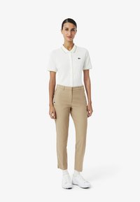Polo bianca con dettagli verdi sul colletto, abbinata a pantaloni beige su misura. Le scarpe sono bianche con un design minimalista. Entrambi gli indumenti presentano un logo.