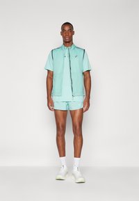 Lightweight mint green athletic outfit featuring a zippered vest, short sleeves, and shorts. Accented with reflective detailing and logo.