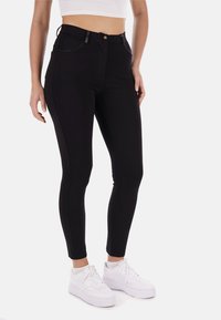 Leggings neri a vita alta con una vestibilità slim, realizzati in un tessuto elasticizzato, con tasche frontali e cuciture a contrasto. Indossati con sneakers bianche.