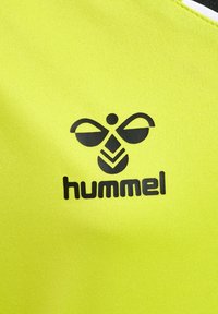 Lyst gul sportswear stof med et sort logo-design, der indeholder cirkulære og linære elementer, samt ordet "hummel" i fed skrift.