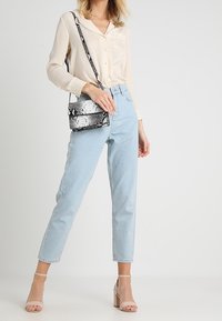 Béžová košile na knoflíky, světle modré džíny s vysokým pasem, růžové sandály na blokovém podpatku a kabelka přes rameno s černo-bílým hadím vzorem.