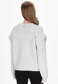 Lys grå strikket sweater med en afslappet pasform, der har ribbet kant og sænkede skuldre. Blød tekstur, simpelt design, ingen synlige mønstre.
