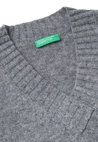 Suéter gris de punto con cuello en V y ribete acanalado, con etiqueta verde que dice "United Colors of Benetton" en el interior del cuello.