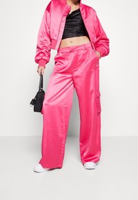 Rosa satinbombarjacka som matchas med vida cargobyxor med fickor, bärs med vita sneakers och en liten svart handväska.