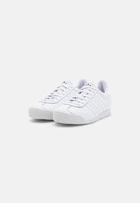 Bílé tenisky s hladkým koženým svrškem, semišovou špičkou, šesti průchodkami a třemi bočními pruhy. Gumová podrážka s texturovaným vzorem běhounu.