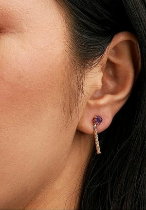 Ohrringe in Goldoptik mit einem lila Edelstein an der Spitze und einem hängenden Kettendesign, das eine glatte Textur und geometrische Form zeigt.