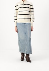 Cremfarbener Pullover mit schwarzen horizontalen Streifen und hohem Kragen, kombiniert mit einem hellblauen Jeans-Maxirock und braunen Stiletto-Ankle-Boots.