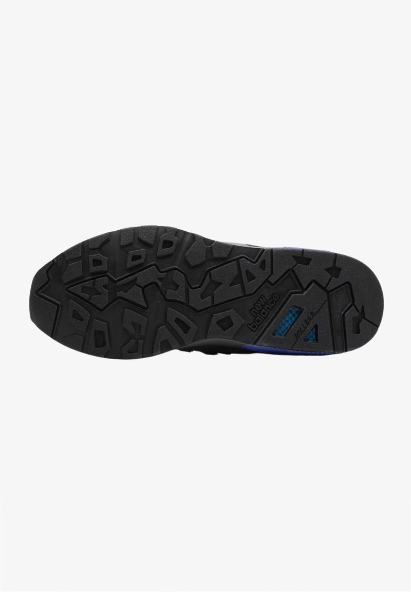 Semelle de chaussure de sport noire présentant un motif de semelle rugueux, avec la marque "New Balance" visible. Comprend une surface texturée et des accentuations de couleur.