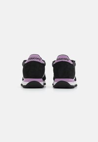 Sneaker in suede nero con un tallone viola e una suola bianca. Presenta una striscia bianca a contrasto laterale. Design minimalista.