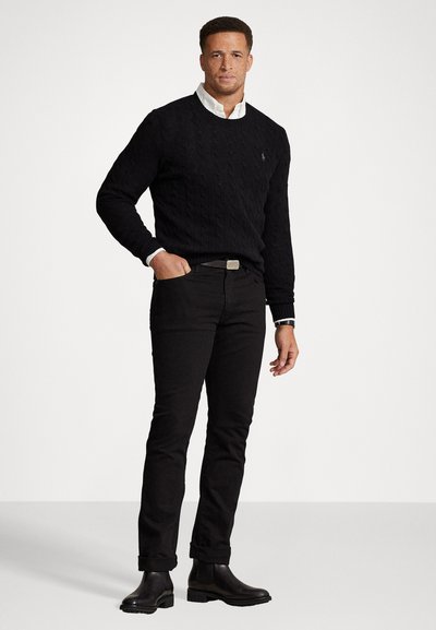 Crni pulover s pletenim uzorkom, bijela košulja ispod, crne traperice i crne kožne čizme do gležnja. Jednostavan dizajn s rebrastom teksturom.