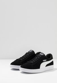 Black suede sneakers with white rubber soles, featuring laces and a white Puma logo on the side and tongue. Smooth texture overall.