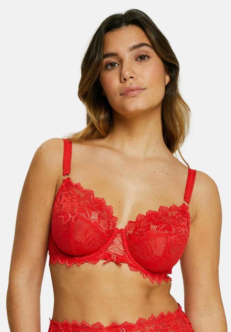 Soutien-gorge en dentelle rouge avec un design en scallop, des bonnets transparents, des bretelles réglables et un embellissement au centre.