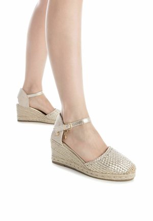 Espadrillas con zeppa e superiore in tessuto metallico intrecciato, suola intermedia in juta naturale e cinturino alla caviglia con fibbia dorata e dettaglio a ciondolo.