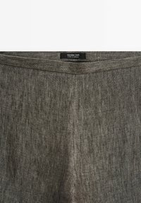 Tissu en lin gris avec une couture centrale et une étiquette noire indiquant Massimo Dutti Made in Morocco sur le bord supérieur.