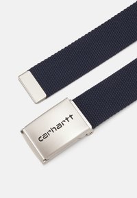 Cintura intrecciata blu navy con fibbia metallica argentata embossata con "carhartt". La texture è resistente e il design è semplice e funzionale.