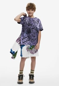 Purple graphic t-shirt featuring comic designs, paired with white tie-dye shorts in blue, green, and purple. Brown boots complete the look.