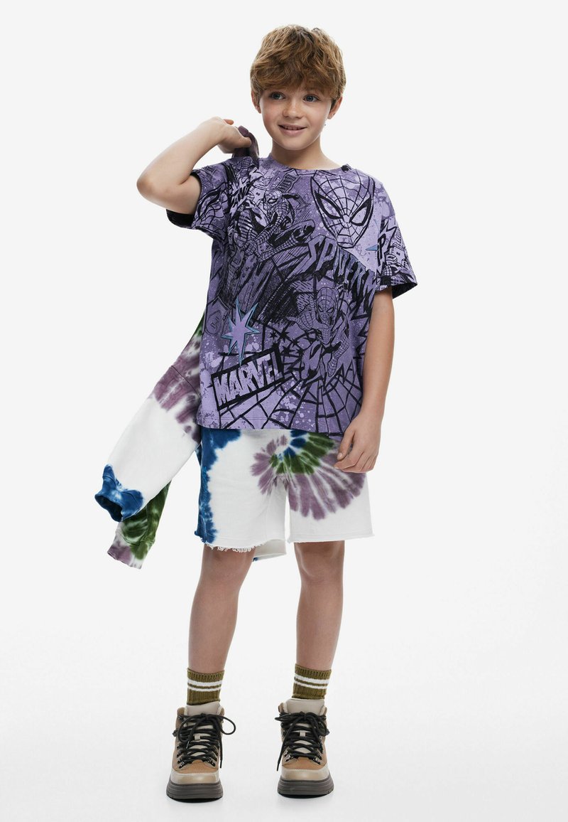 Purple graphic t-shirt featuring comic designs, paired with white tie-dye shorts in blue, green, and purple. Brown boots complete the look.