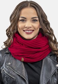 Rød strikket uendelighedsscarf med et struktureret mønster, suppleret af et brunt lædermærke. Båret med en sort læderjakke.