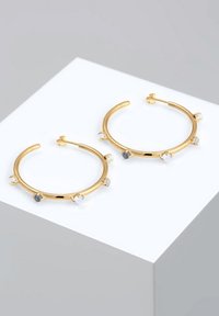Guld hoop øreringe med fem dekorative sten i klare og dæmpede blå nuancer. Designet har en glat overflade og en cirkulær form.