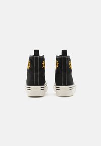 Sorte høye sneakers med gult solbroderi, hvit såle med svarte striper, og trekkspill bak. Materiale i bomullscanvas.