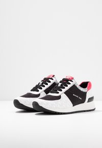 Svarta och vita sneakers med mesh-textil, läderdetaljer och rosa accenter. Har ett texturerat mönster och en gummisula.