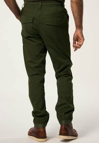 Pantalones de color verde oliva con cintura elástica y puños acanalados, que cuentan con dos bolsillos traseros y una tela suave y ligeramente texturizada. Zapatos marrones visibles.