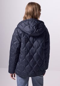 Giacca puffer navy trapuntata con cappuccio, caratterizzata da un motivo testurizzato di forme ovali. Ha maniche lunghe e una vestibilità comoda.