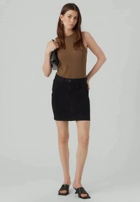 Jupe mini en denim noir avec une fermeture à boutons et cinq poches, associée à un débardeur ajusté en cotton côtelé marron et des sandales à glissière noires.