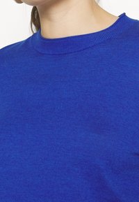 Blauer Baumwollpullover mit rundem, geripptem Ausschnitt und glatter Textur, Nahaufnahme des Stoffes und Kragenbereichs.