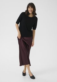 Top nero a maniche corte abbinato a una gonna fluida in satin bordeaux e scarpe basse nere, con un design semplice e lineare.