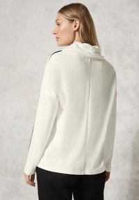 Witte lange mouwen top van gladde stof met een col, voorzien van zwarte zijstrepen en een rechte achternaad.