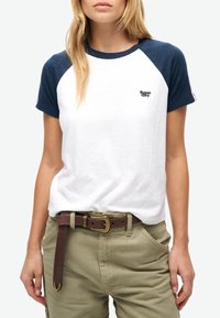 Hvid bomulds t-shirt med marineblå raglanærmer og et lille broderet logo. Bæres med grønne cargo bukser og et brunt bælte.