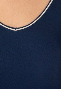 Top in tessuto ribbed blu navy con scollatura rotonda, caratterizzato da un sottile accento argentato lungo il bordo. Texture liscia e design aderente.