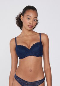 Granatowy koronkowy stanik z fiszbinami, falbaniastymi krawędziami i regulowanymi ramiączkami. W komplecie z dopasowanym zestawem koronkowej bielizny z delikatnym wykończeniem.