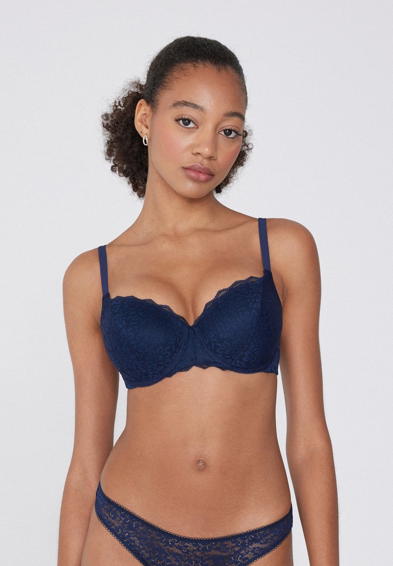 Granatowy koronkowy stanik z fiszbinami, falbaniastymi krawędziami i regulowanymi ramiączkami. W komplecie z dopasowanym zestawem koronkowej bielizny z delikatnym wykończeniem.