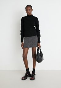 Pulover negru din tricot cu guler înalt, fustă mini din denim gri cu detalii cu ochiuri, geantă de mână din piele neagră și pantofi maro închis cu curea.