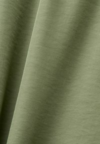 Tissu vert olive doux avec un tissage diagonal et des plis doux créant des ombres subtiles et une texture délicate.