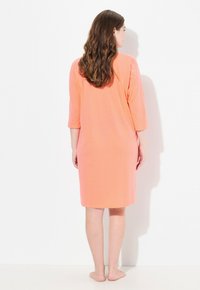 Koronkowa nocna sukienka w kolorze koralowym z rękawami o długości trzech czwartek, wykonana z miękkiego materiału. Posiada subtelne białe kropki oraz luźny krój.