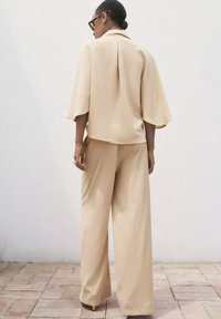 Beige, löst sittande outfit med en kortärmad topp med krage och vida byxor, tillverkad av släckt tyg med en lätt glans.