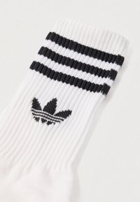 Fehér atlétikai zokni bordázott textúrával, tetején két fekete csíkkal és egy fekete hímzett Adidas trefoil logóval.