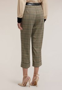 Zielone, zwężane spodnie w kratę o przyciętej długości i podwiniętych mankietach, zestawione z cielistymi szpilkami z paskiem.