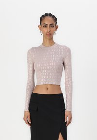 Rosa langermet crop topp med et gjentakende logomønster i ribbete tekstur, sammen med et svart skjørt med sidespalte og lomme.