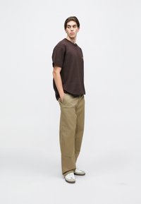 Brown short-sleeve T-shirt with a small logo, paired with light khaki wide-leg pants. White sneakers with gray accents. Slim fit and minimalistic design.