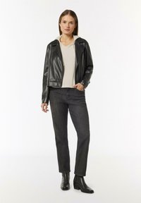 Schwarze Leder-Motorradjacke, beigefarbener Kapuzenpullover, dunkle Jeans und schwarze Knöchelstiefel. Hinweis: die Jacke hat Reißverschlussdetails und eine taillierte Passform.